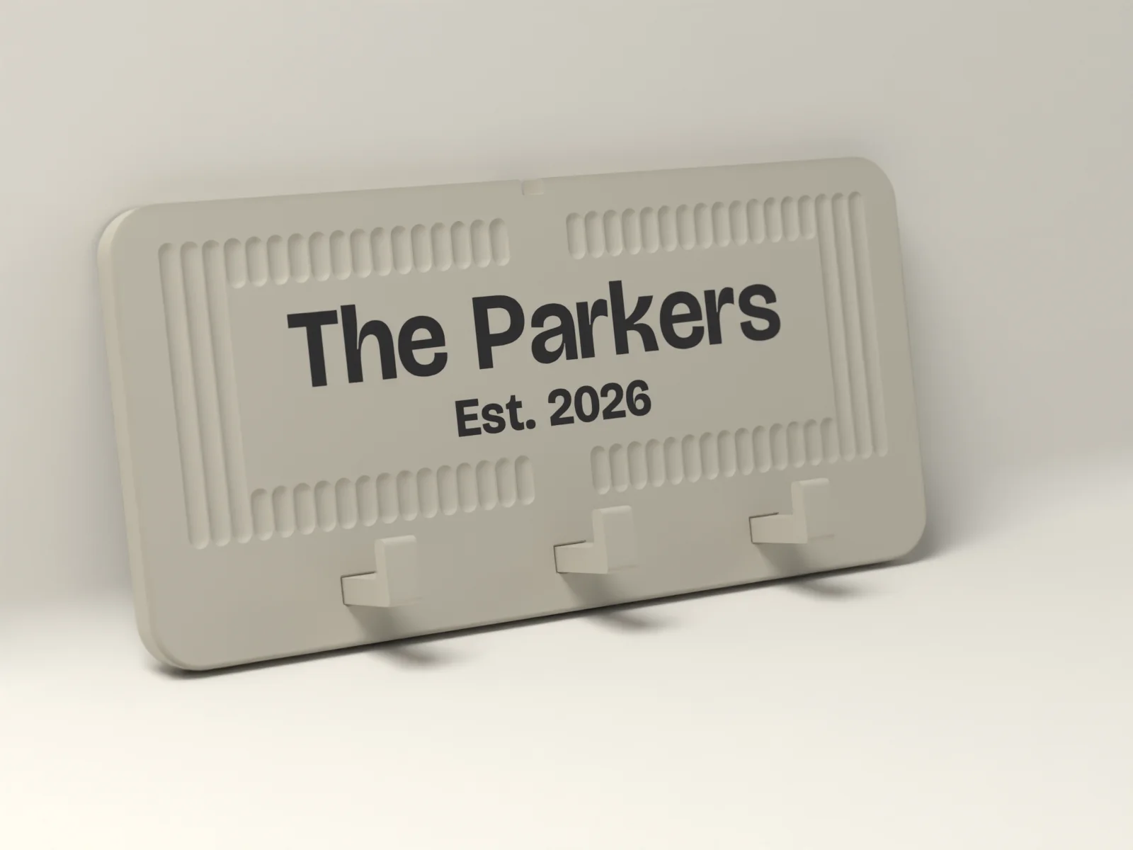 Wall key holder in Bone with The Parkers and Est. 2026 inlaid flush in Ink, framed by fine reeding, with three hooks along a plain rail