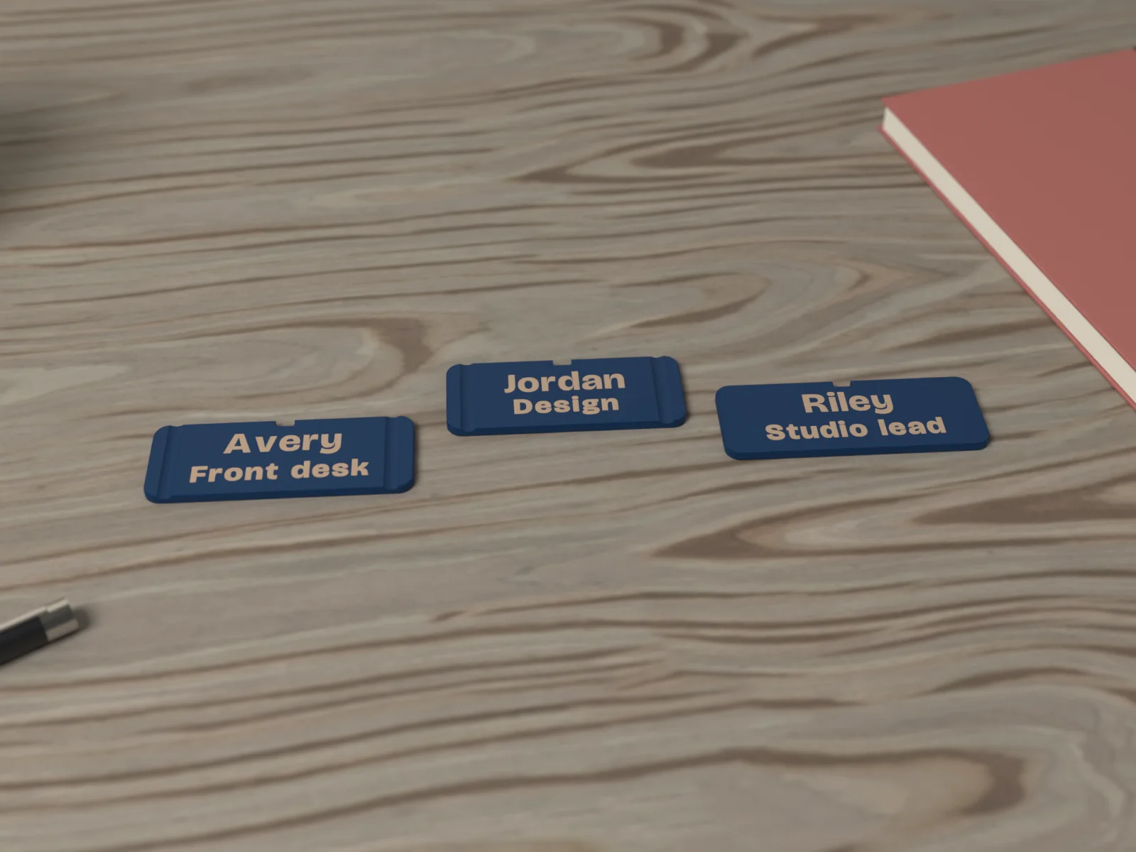 Navy name badges with gold lettering on a walnut desk beside a notebook, a pen and a mug